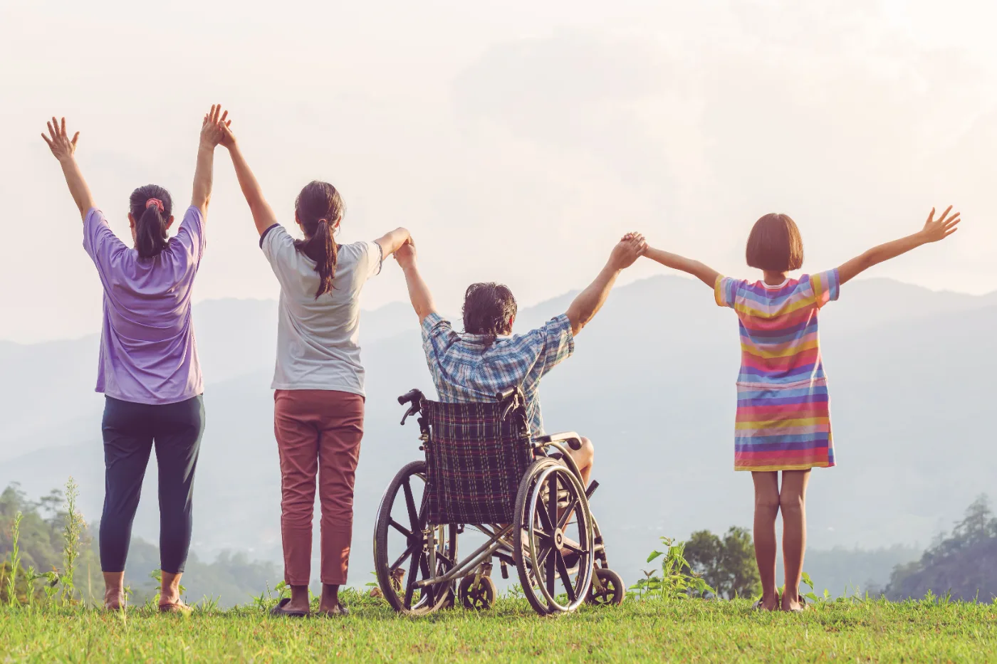 A group of people, one using a wheelchair, raising their hands together looking out over hills