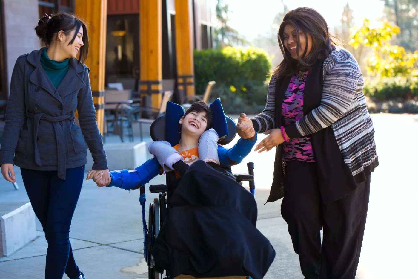 Two support workers walking outdoors with a young person in a wheelchair